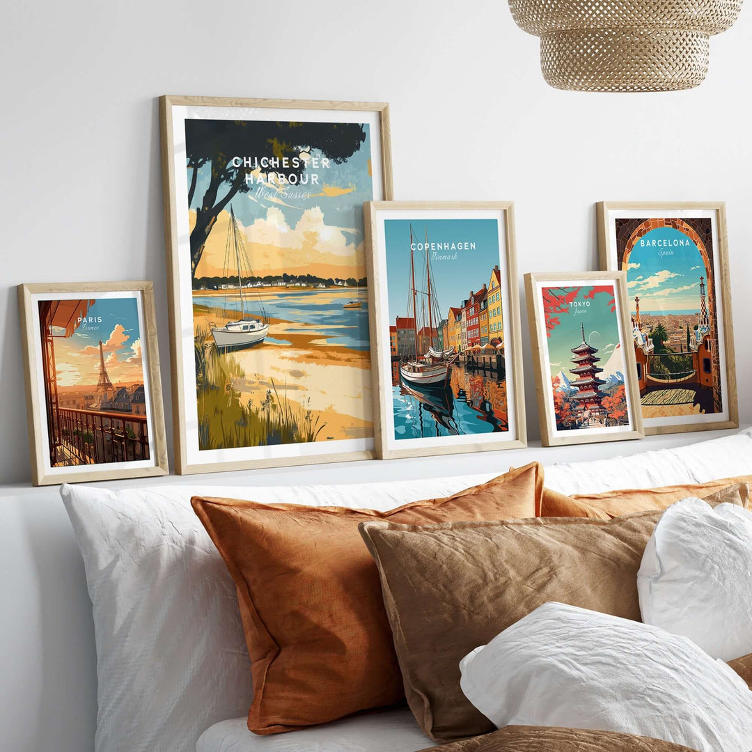 Framed travel prints of Chichester Harbour and other destinations displayed on a cozy bed with decorative pillows.