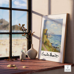 Claude Monet Art Print - Coastal Cliff Path Seascape Wall Art displayed on a wooden table by a window.