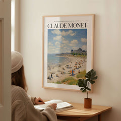Claude Monet Sunny Beach Day Wall Art - Coastal Resort Scene Print hanging in a cozy room with a woman reading