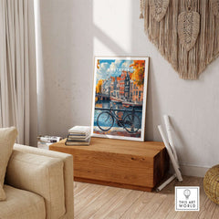 Colorful Amsterdam Canal House Poster - Classic Dutch Canal Scene Print on display in a cozy room with a bicycle.
