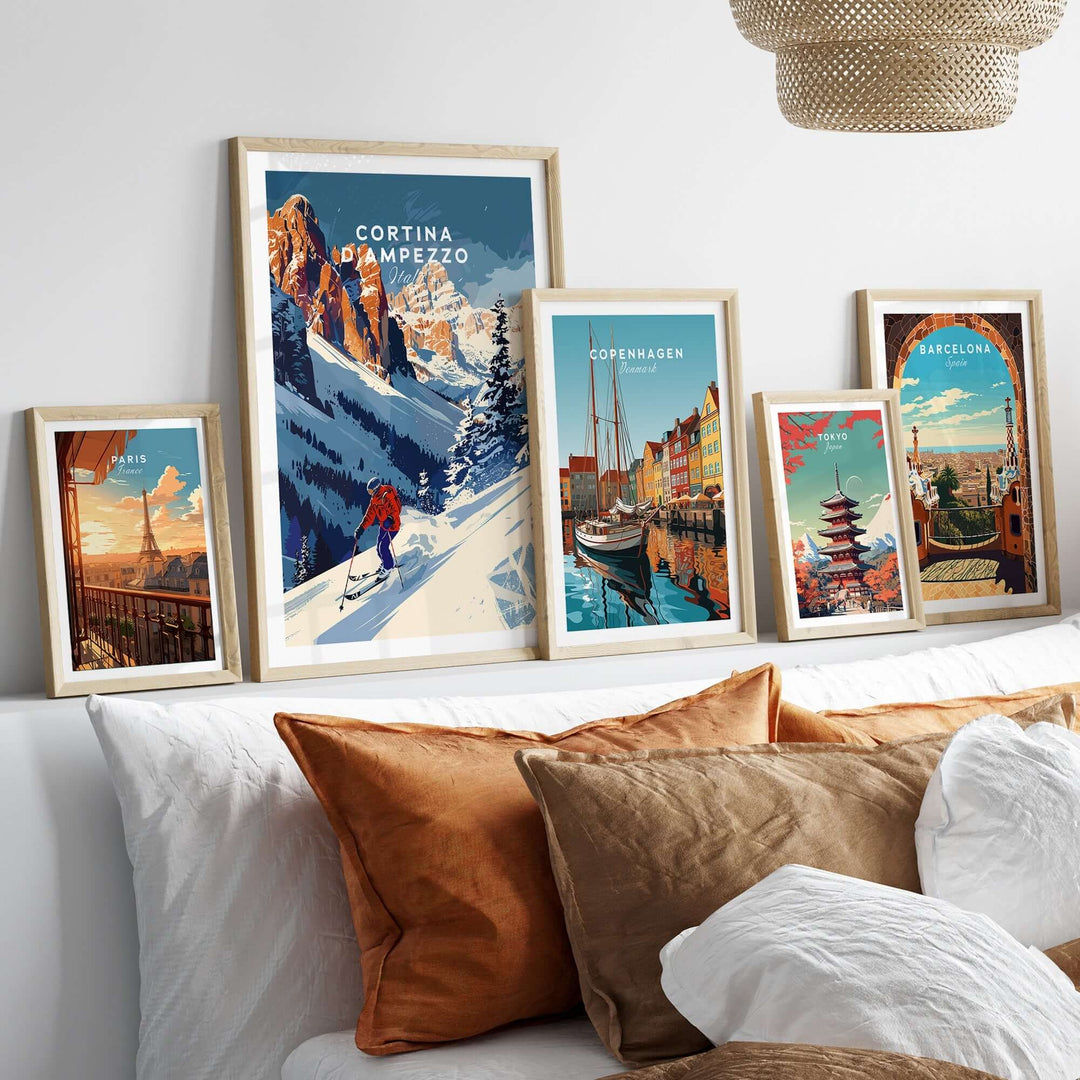 Framed travel posters of Cortina d'Ampezzo, Copenhagen, and Barcelona displayed on a cozy bed with decorative pillows.