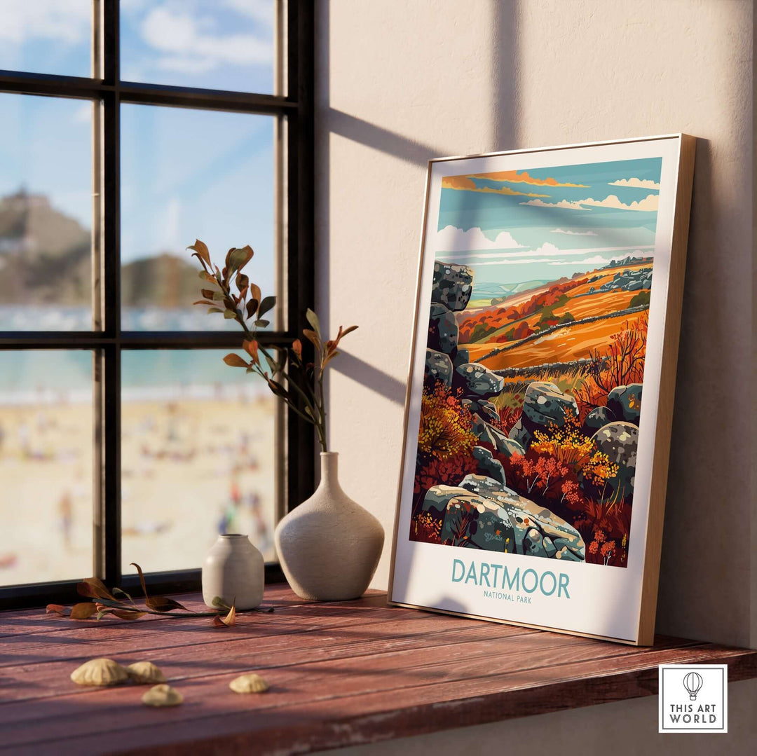 Framed Dartmoor National Park print on a wooden table with a scenic view outside the window, showcasing autumn colors.