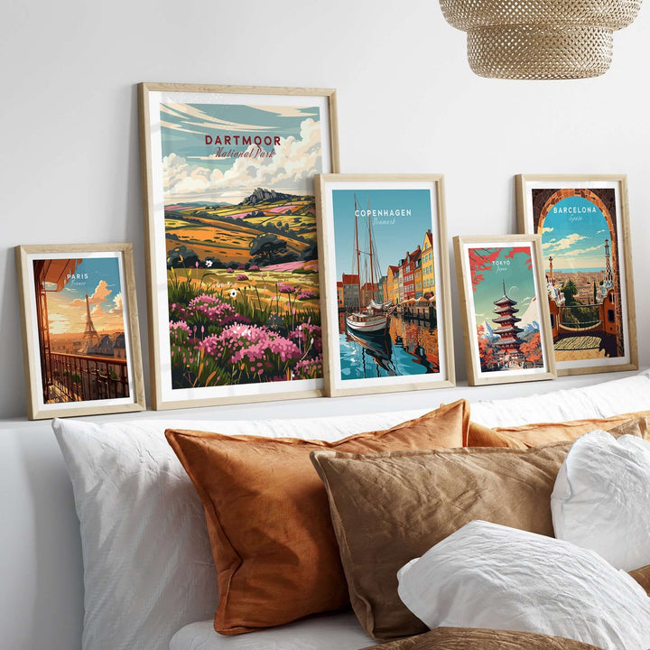 Dartmoor travel print displayed among framed city prints on a cozy bed with decorative cushions.