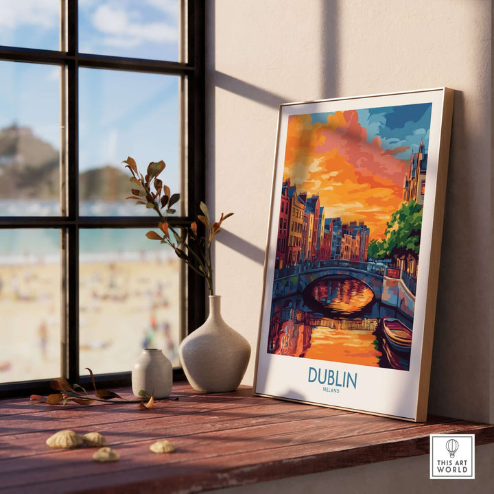 Dublin wall art poster featuring a vibrant sunset over the cityscape, displayed on a wooden shelf by a window.