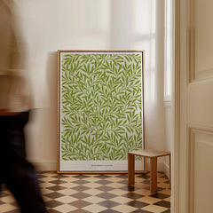 Framed green botanical wall art on checkered floor in bright room, person walking past.