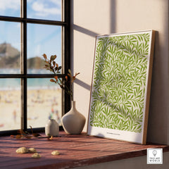 Framed botanical wall art print with green leaf pattern on wood sill beside window with beach view.