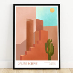Moroccan architecture wall art print with geometric buildings, cactus, sun, and blue sky in a black frame.