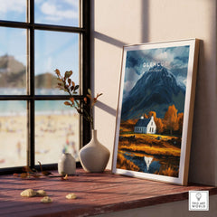 Glencoe Scotland Poster beautifully displayed on a wooden table with a scenic view of mountains and a cozy cottage.