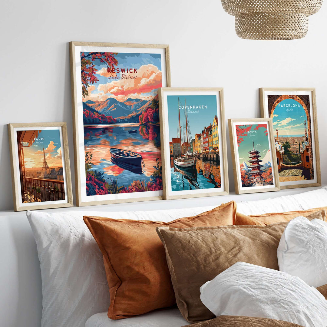 Framed travel prints of Keswick Lake District and other cities on a cozy bed, showcasing vibrant landscapes and cultural scenes.