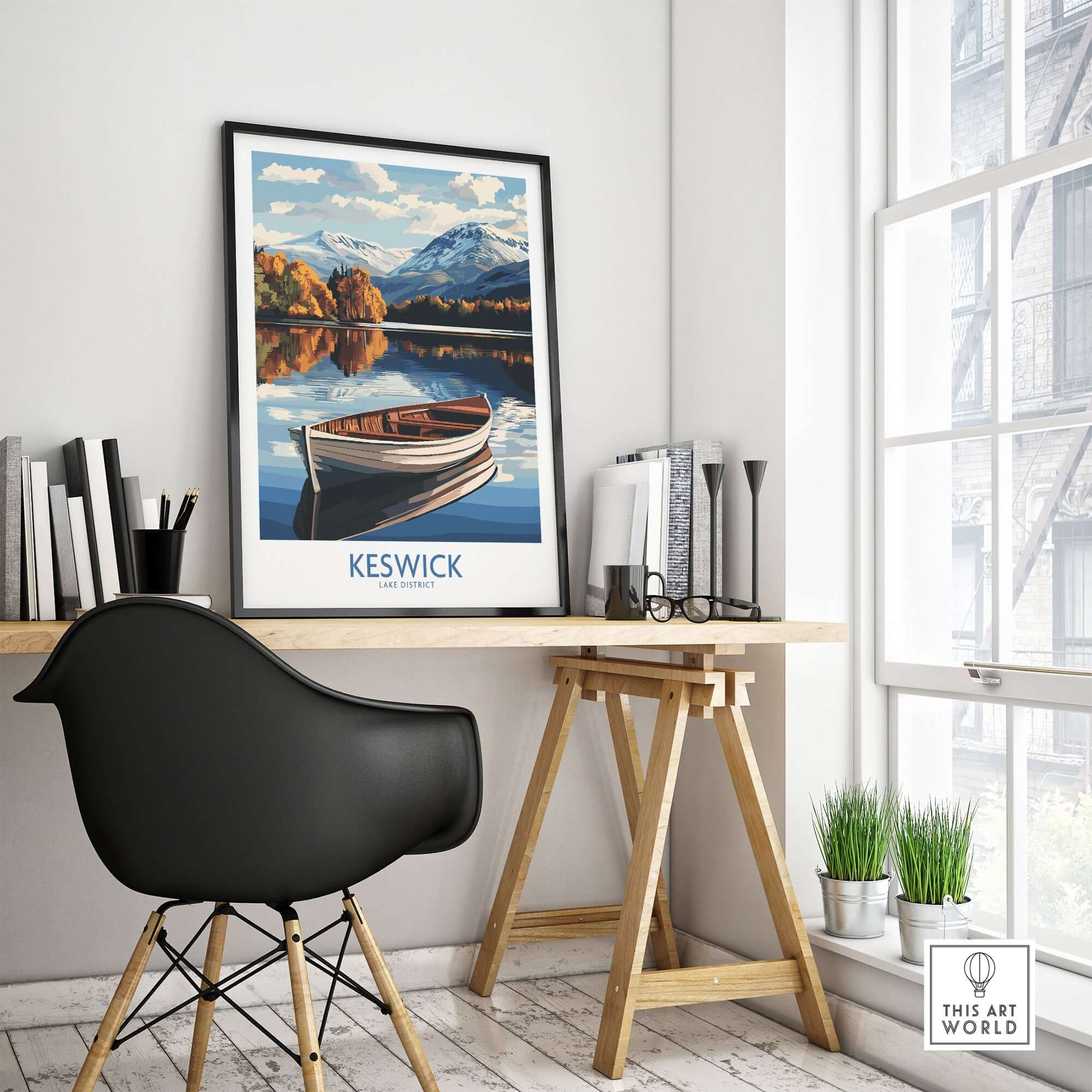 Keswick Poster Lake District framed on a wall above a workspace with a boat and mountain scenery.