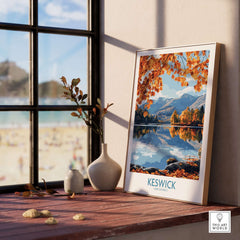 Keswick Travel Poster featuring autumn scenery in the Lake District, framed and displayed on a wooden shelf.
