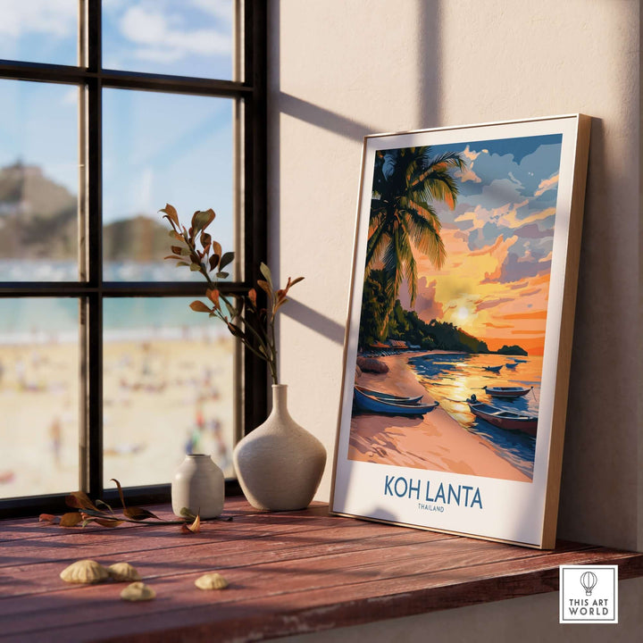 Koh Lanta travel poster displayed on a windowsill, showcasing a serene beach scene with sunset and boats.