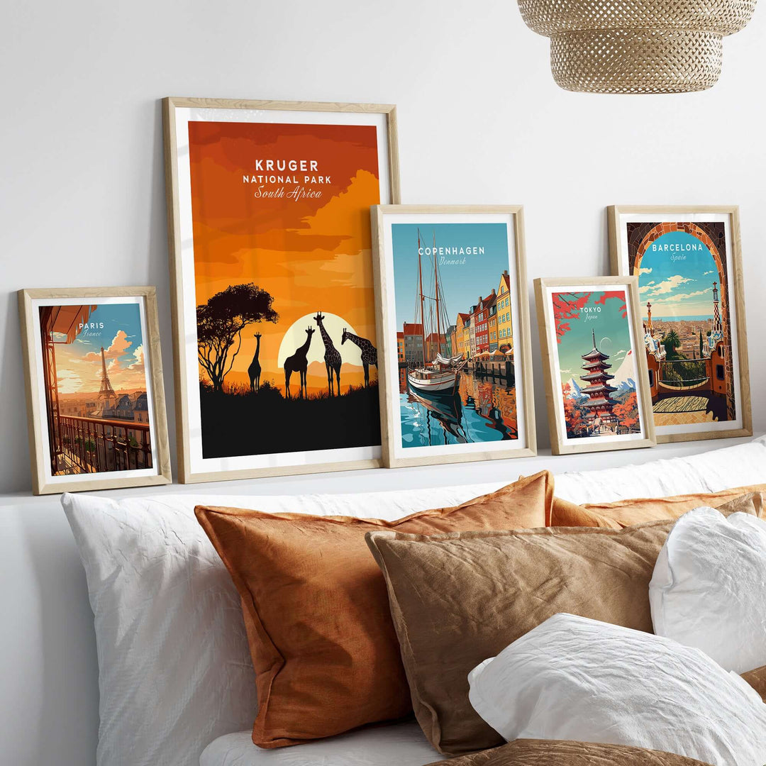 Display of framed travel art prints, including Kruger National Park giraffe silhouette against sunset.