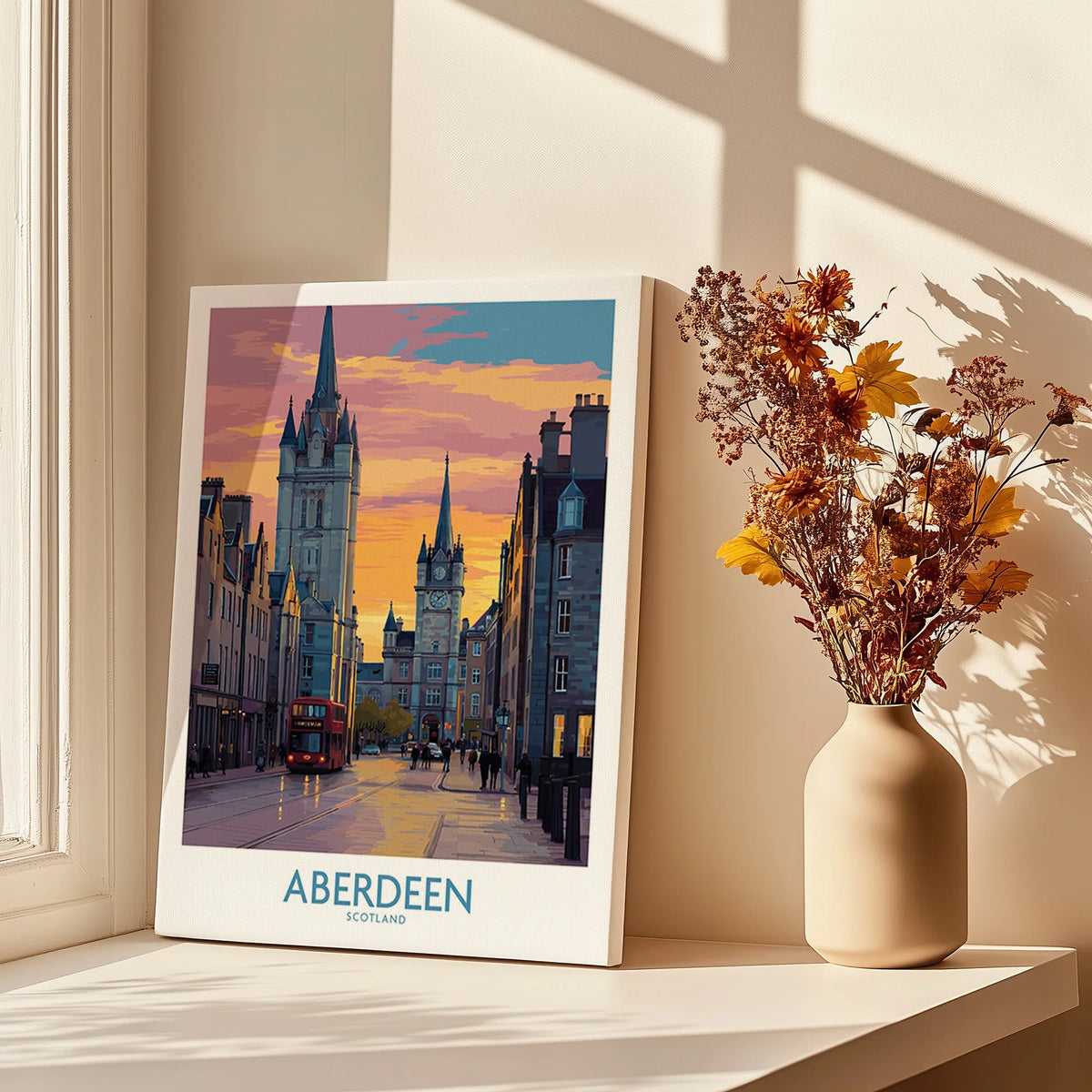Aberdeen Scotland travel poster with city skyline, red bus, and sunset, displayed on windowsill with dried flowers.