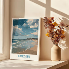 Aberdeen Scotland travel poster print with beach, lighthouse, and clouds, styled on windowsill with dried flowers.