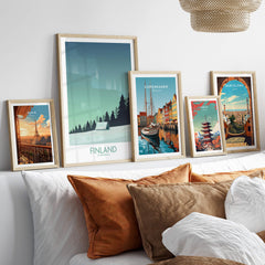 Finland Print Travel Poster displayed among other travel posters on a stylish couch with decorative pillows.