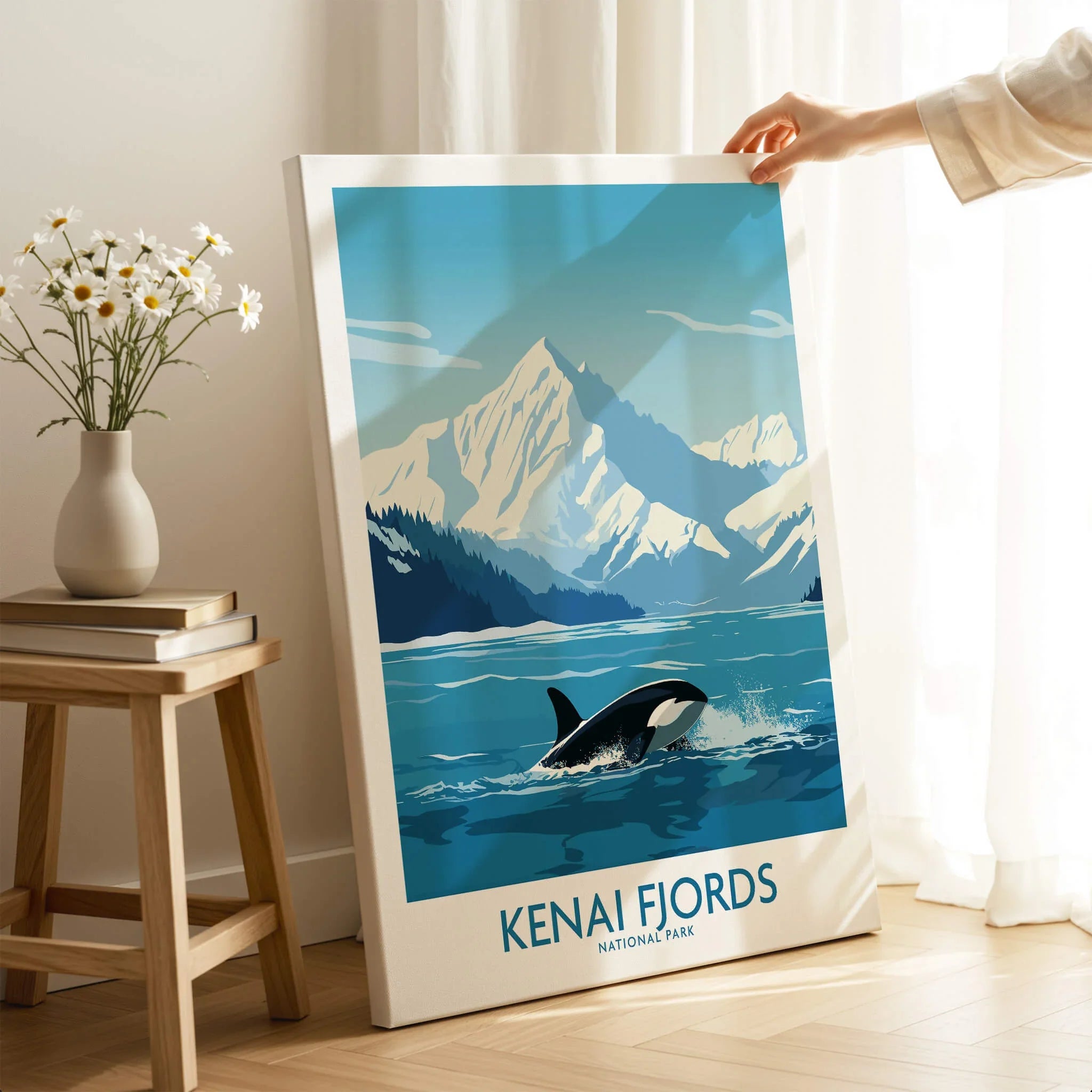 Hand holding Kenai Fjords National Park travel poster with orca and mountains in bright room