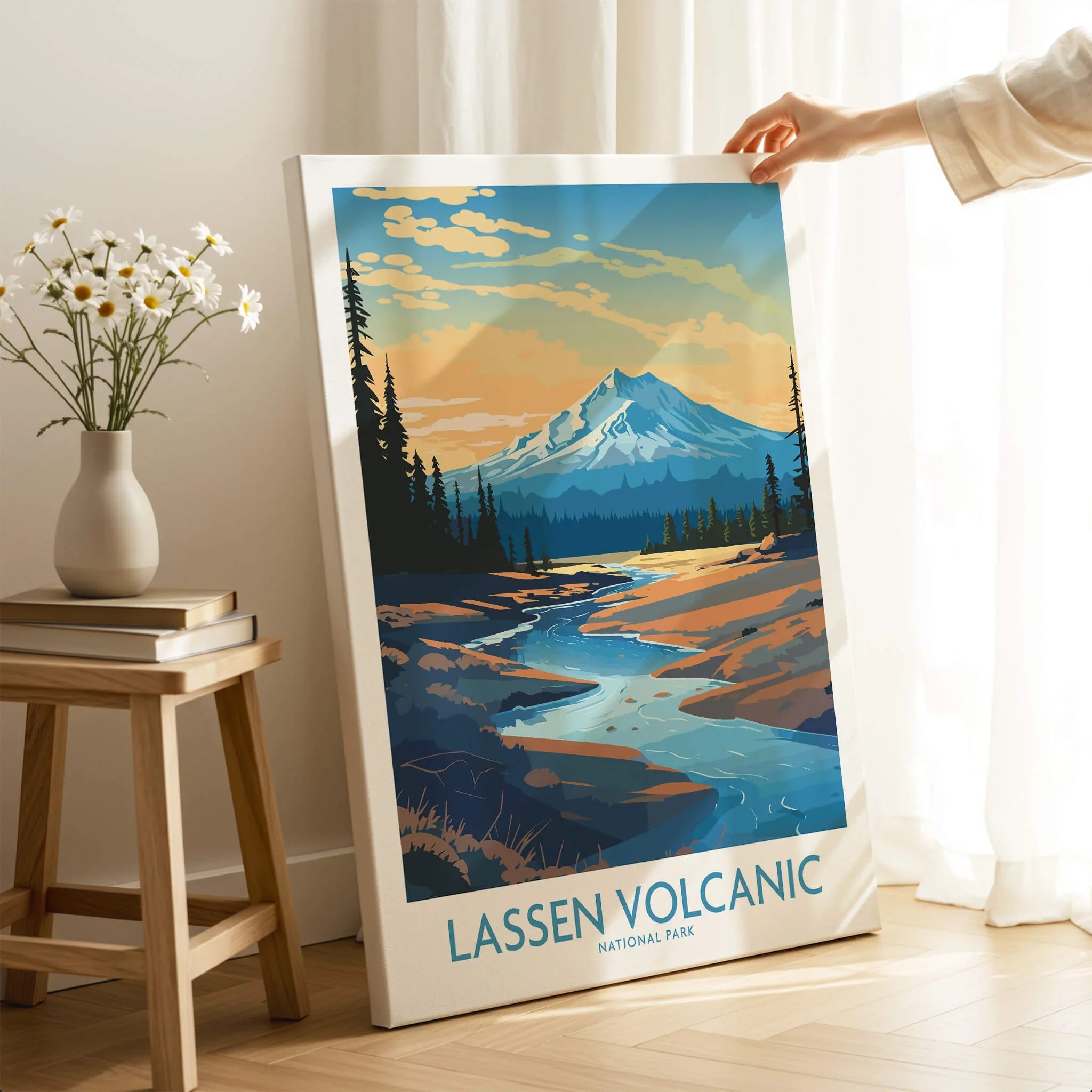 Hand holding Lassen Volcanic National Park art print in cozy room with flowers and books