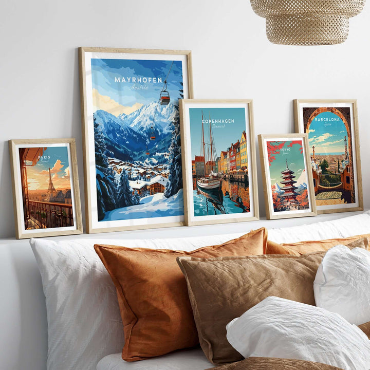 Framed travel prints including Mayrhofen, Copenhagen, and Barcelona displayed on a cozy sofa with decorative pillows.