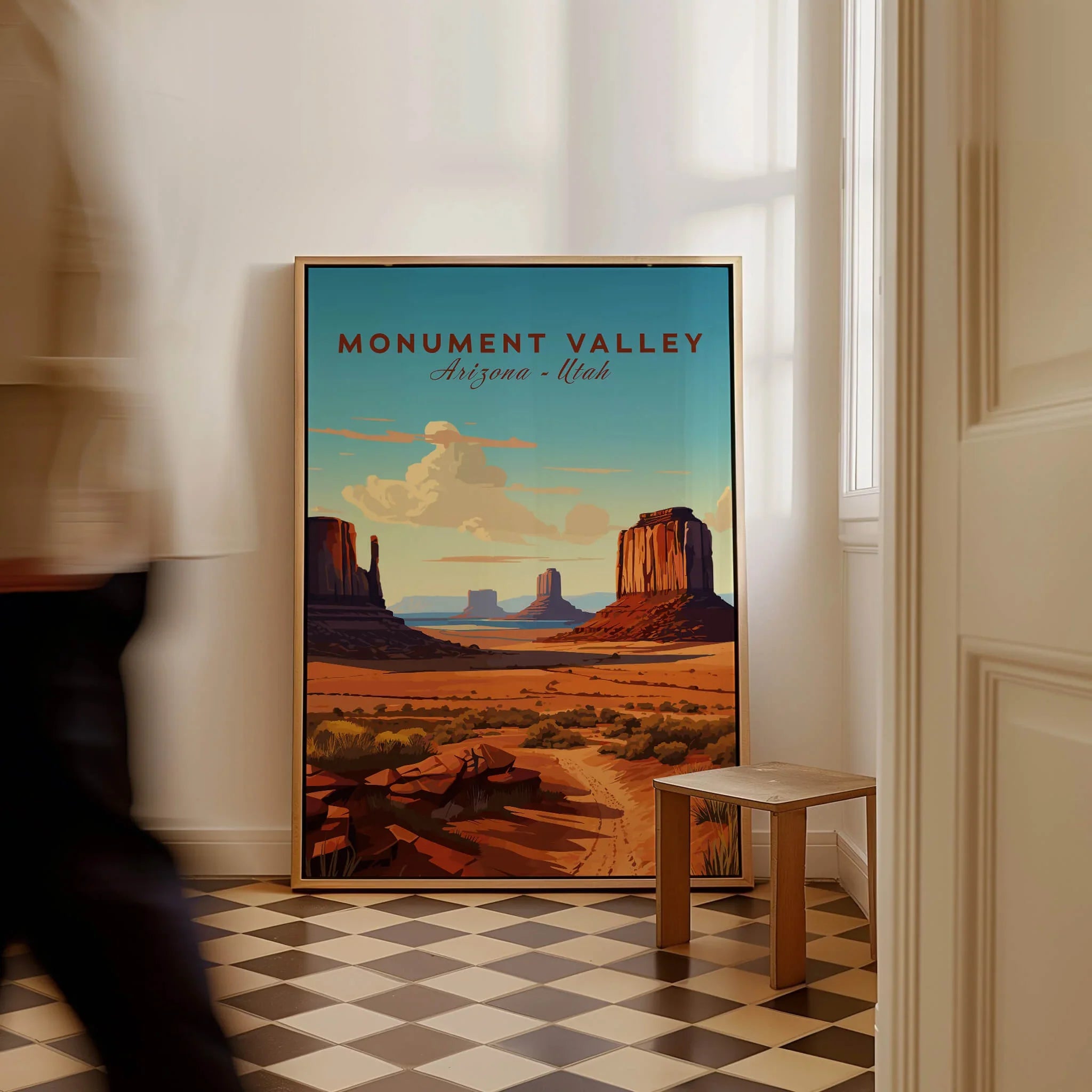 Framed Monument Valley travel poster on floor in sunlit room with checkered tiles.