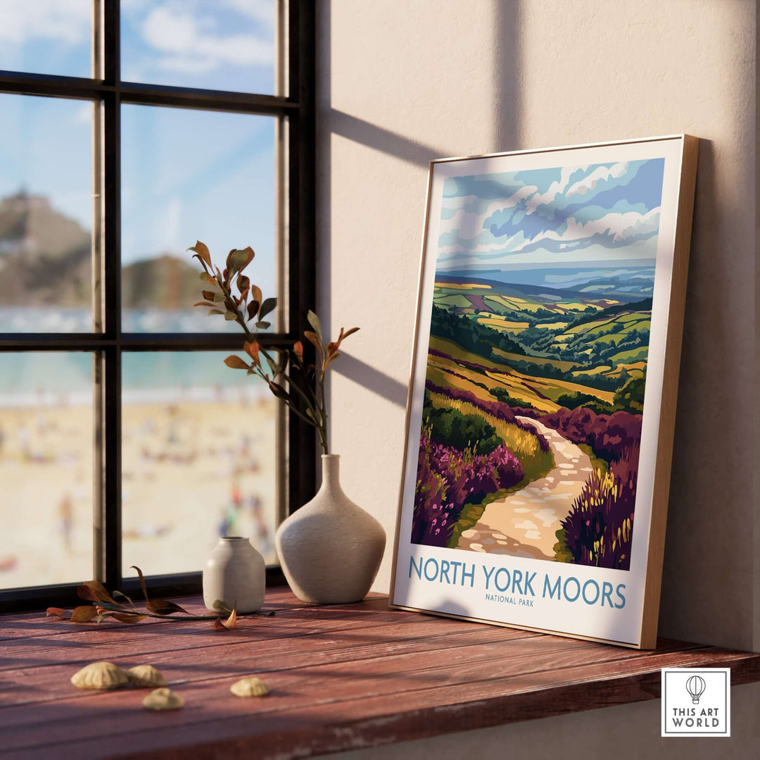 Vibrant North York Moors National Park poster displayed on a windowsill with a beach view in the background.