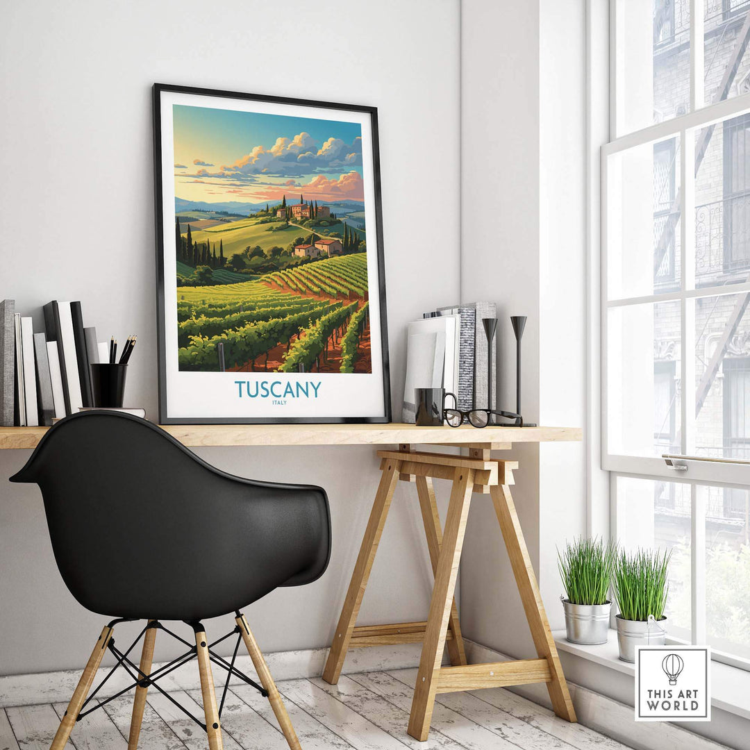 Tuscany wall art print in black frame on a desk in the sunlight in a modern office setting. The travel poster of Tuscany features rolling vineyards and an Italian village on a hill. 