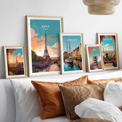 Art prints of Paris, Copenhagen, and Barcelona displayed in stylish frames on a cozy bed backdrop.