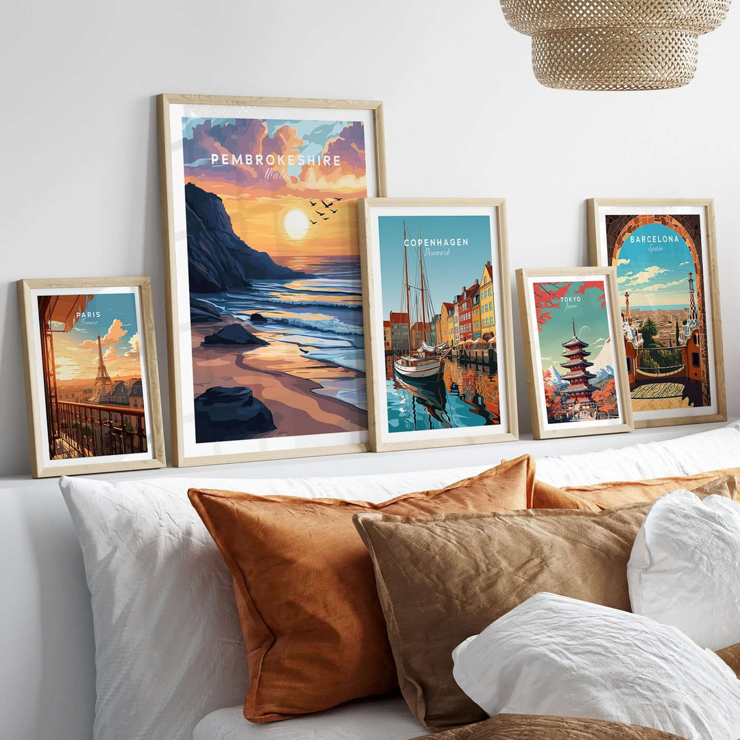 Pembrokeshire Coast travel print framed alongside other travel art on a stylish wall above a cozy bed with decorative pillows.