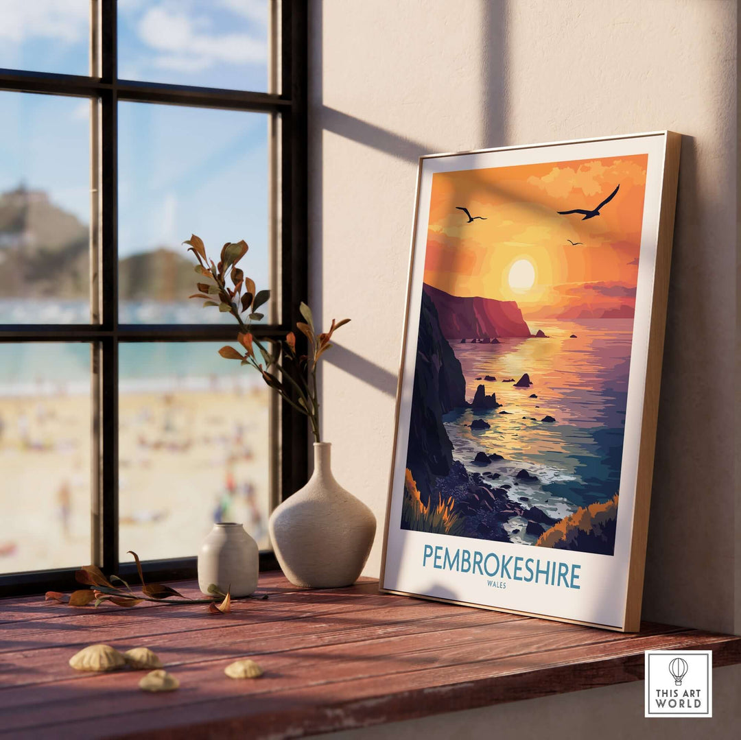 Pembrokeshire Coast wall art print featuring a vibrant sunset view, displayed on a wooden table by the window.