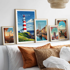 Plymouth Lighthouse Art - Seaside View Travel Poster displayed among other framed travel posters on a decorative bed.