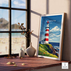 Plymouth Lighthouse Art - Seaside View Travel Poster displayed on a wooden shelf with beach view outside the window.