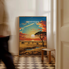 Framed Serengeti National Park travel poster with sunset landscape, on floor in modern room.