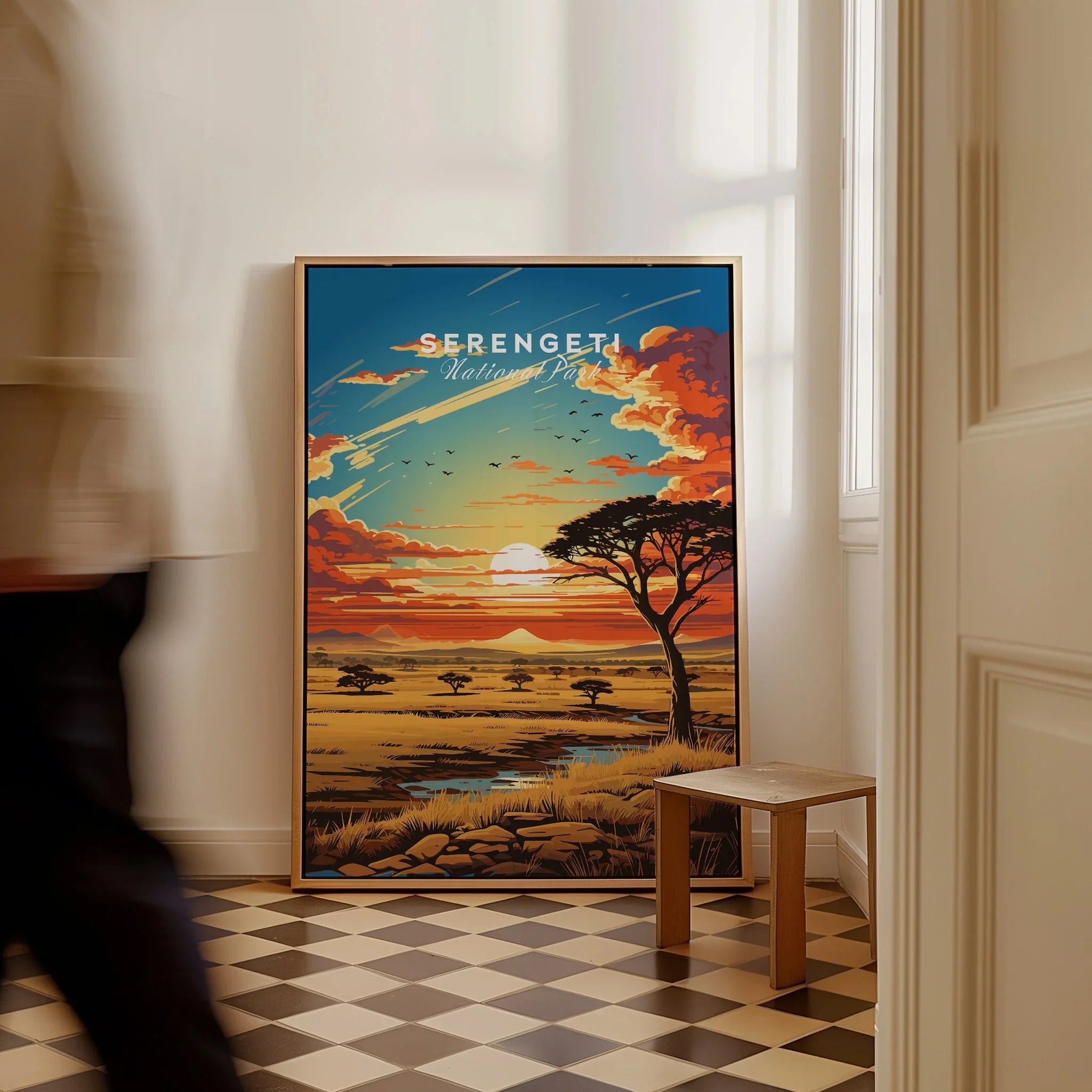 Framed Serengeti National Park travel poster with sunset landscape, on floor in modern room.