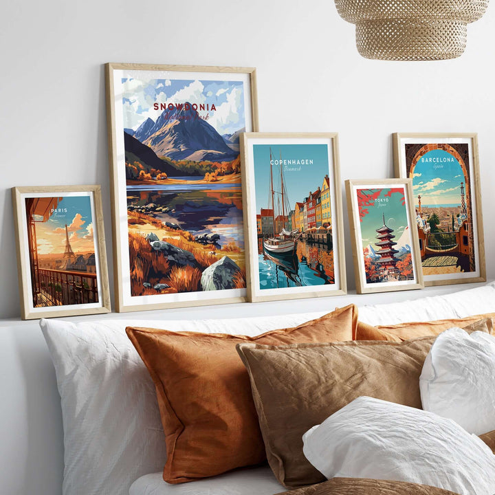 Framed travel art prints including Snowdonia, Copenhagen, and Barcelona displayed above decorative pillows on a stylish bed.