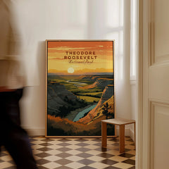 Framed Theodore Roosevelt National Park travel poster with landscape art on floor, man walking past.