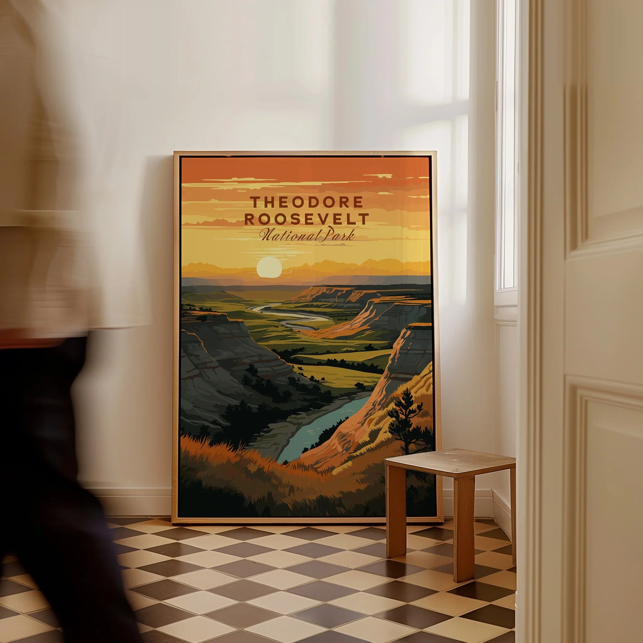 Framed Theodore Roosevelt National Park travel poster with landscape art on floor, man walking past.
