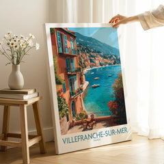 Villefranche-sur-Mer travel art print with coastal view, leaning on floor near vase and books.