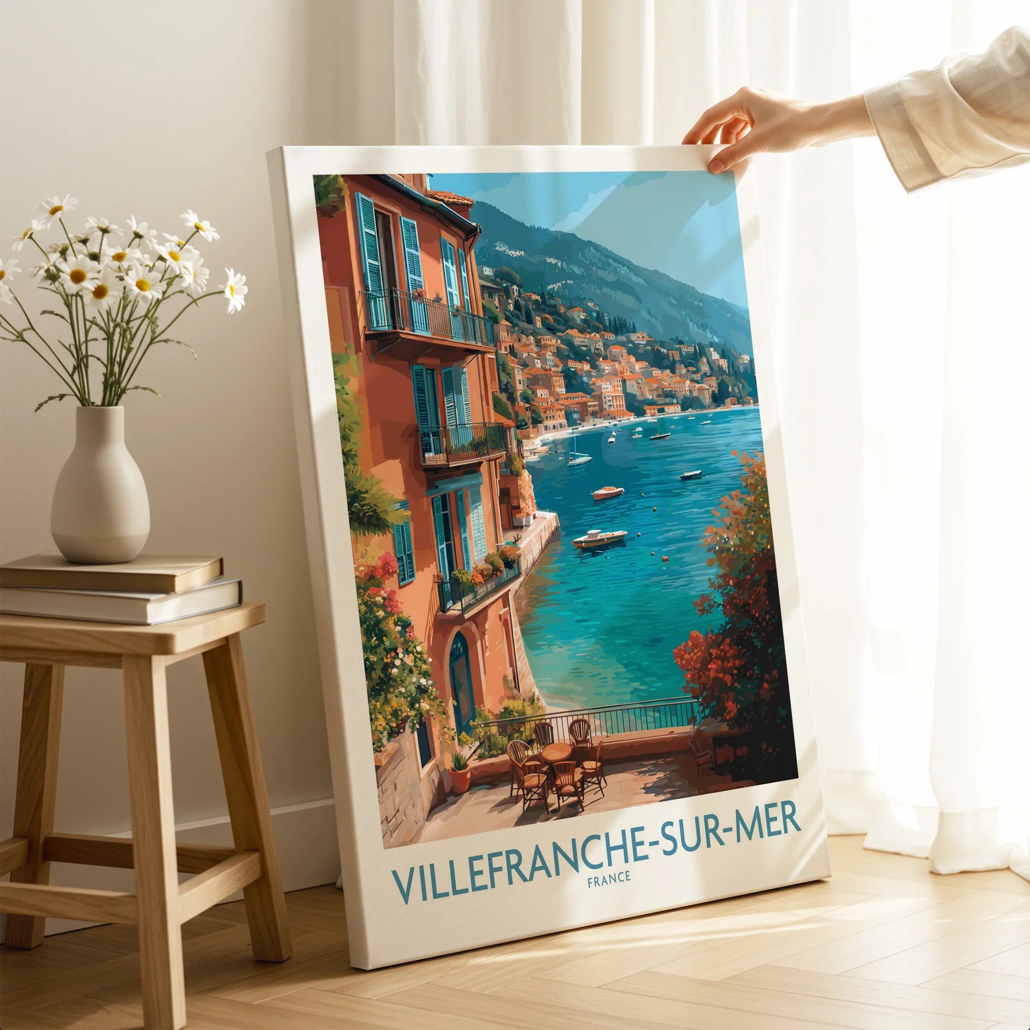Villefranche-sur-Mer travel art print with coastal view, leaning on floor near vase and books.