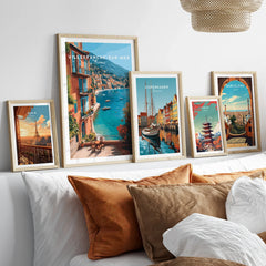 Set of five framed travel art prints featuring Paris, Villefranche-sur-Mer, Copenhagen, Tokyo, and Barcelona above a bed with neutral wood frames.