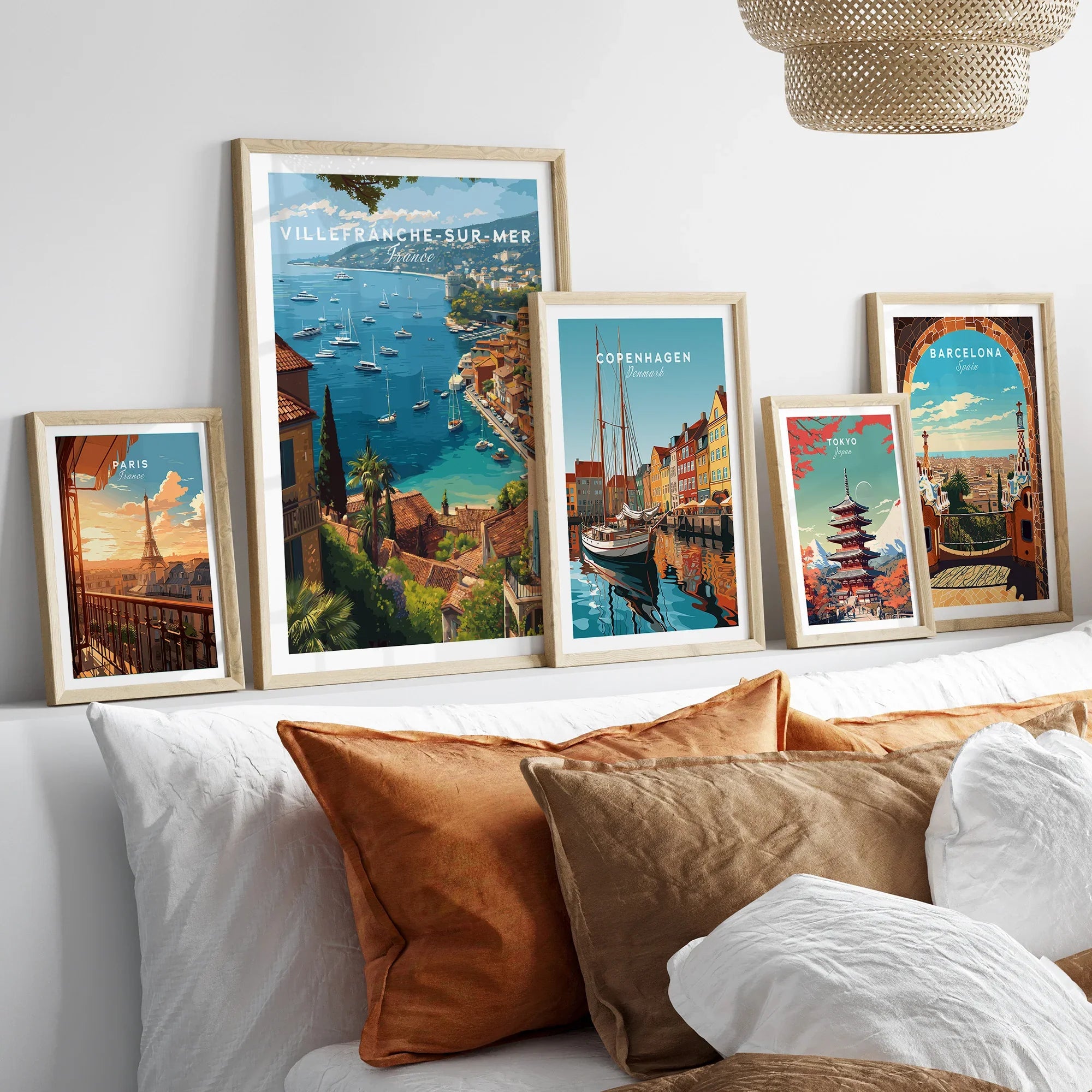 Set of five framed travel posters above bed, featuring Paris, Villefranche-sur-Mer, Copenhagen, Tokyo, and Barcelona.