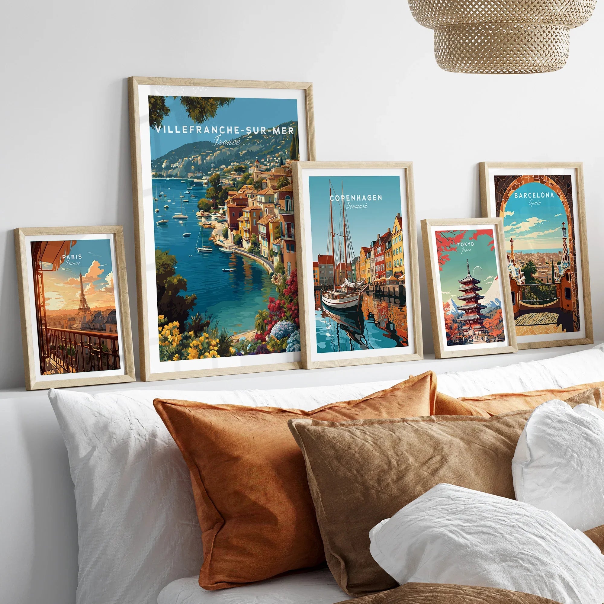 Set of five framed travel art prints above bed showcasing Paris, Villefranche-sur-Mer, Copenhagen, Tokyo, and Barcelona.