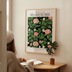 William Morris Prints - Pink Blossom Art Print - Dark Botanical Poster displayed on wall with person reading nearby.
