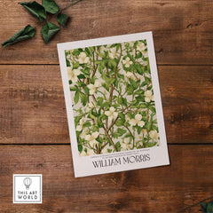 William Morris Prints - White Blossom Branch Art Print - Exhibition Poster on a wooden surface with green leaves.