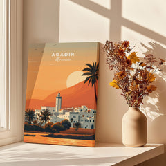 Agadir Travel Poster – Moroccan Mosque and Desert Sunset Art displayed beside a vase of flowers and sunlight.