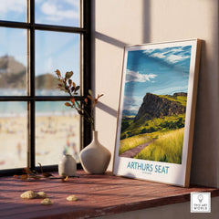 Arthurs Seat Scotland Wall Art Print displayed on a wooden table by a window, showcasing the scenic landscape.