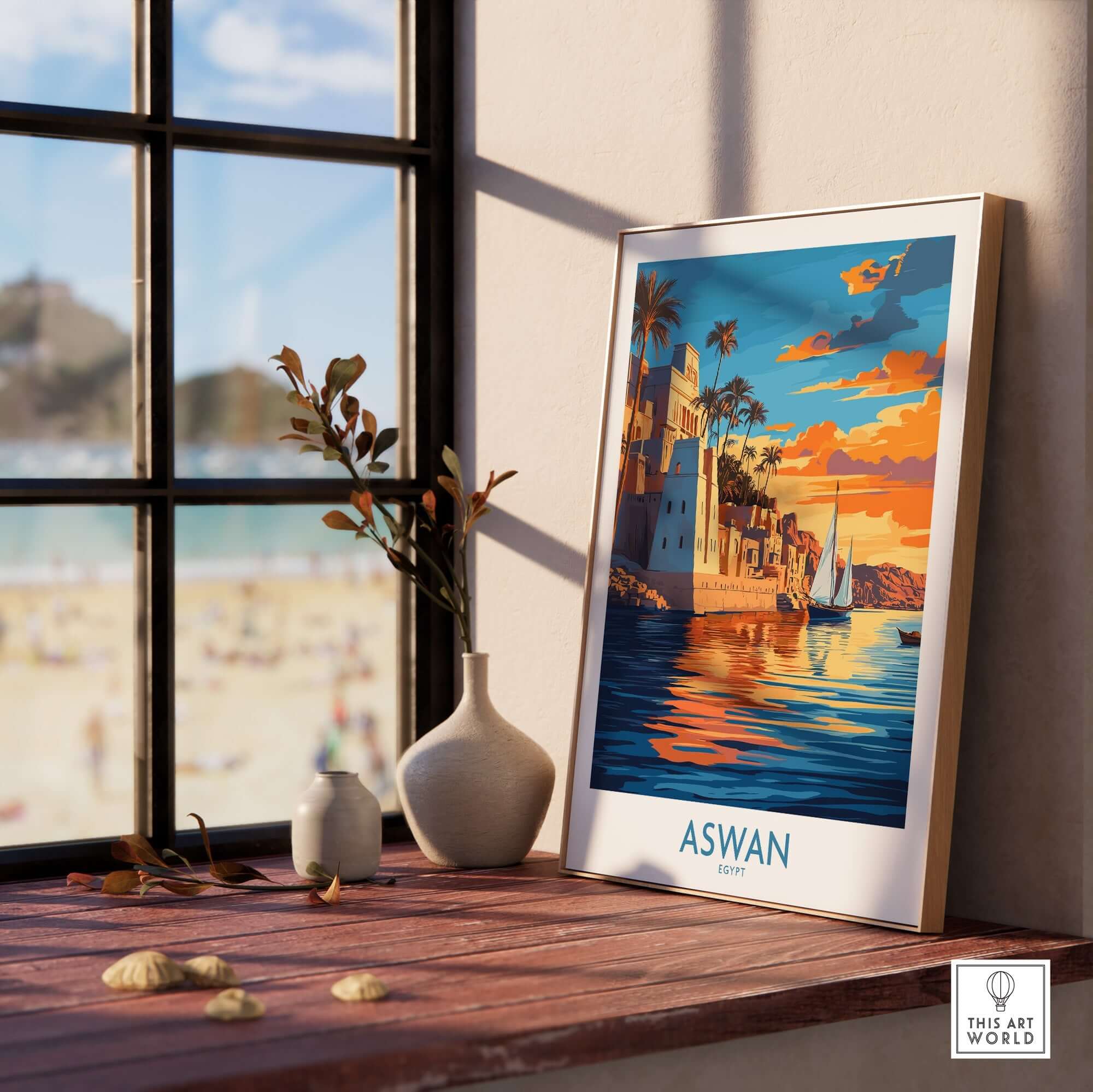 Aswan Travel Poster displayed indoors beside a vase and coastal scenery, capturing the beauty of Aswan in vibrant colors.