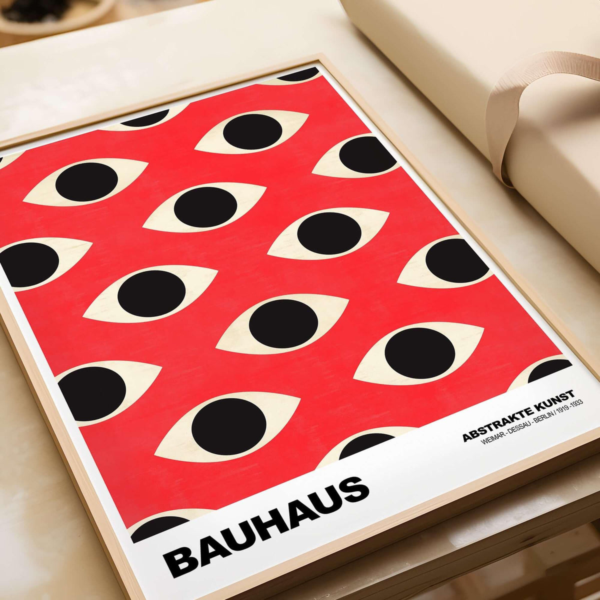 Bauhaus Exhibition Prints - Repeating Eyes Pattern Poster Red Black Cream Art displayed in a stylish frame atop a desk.