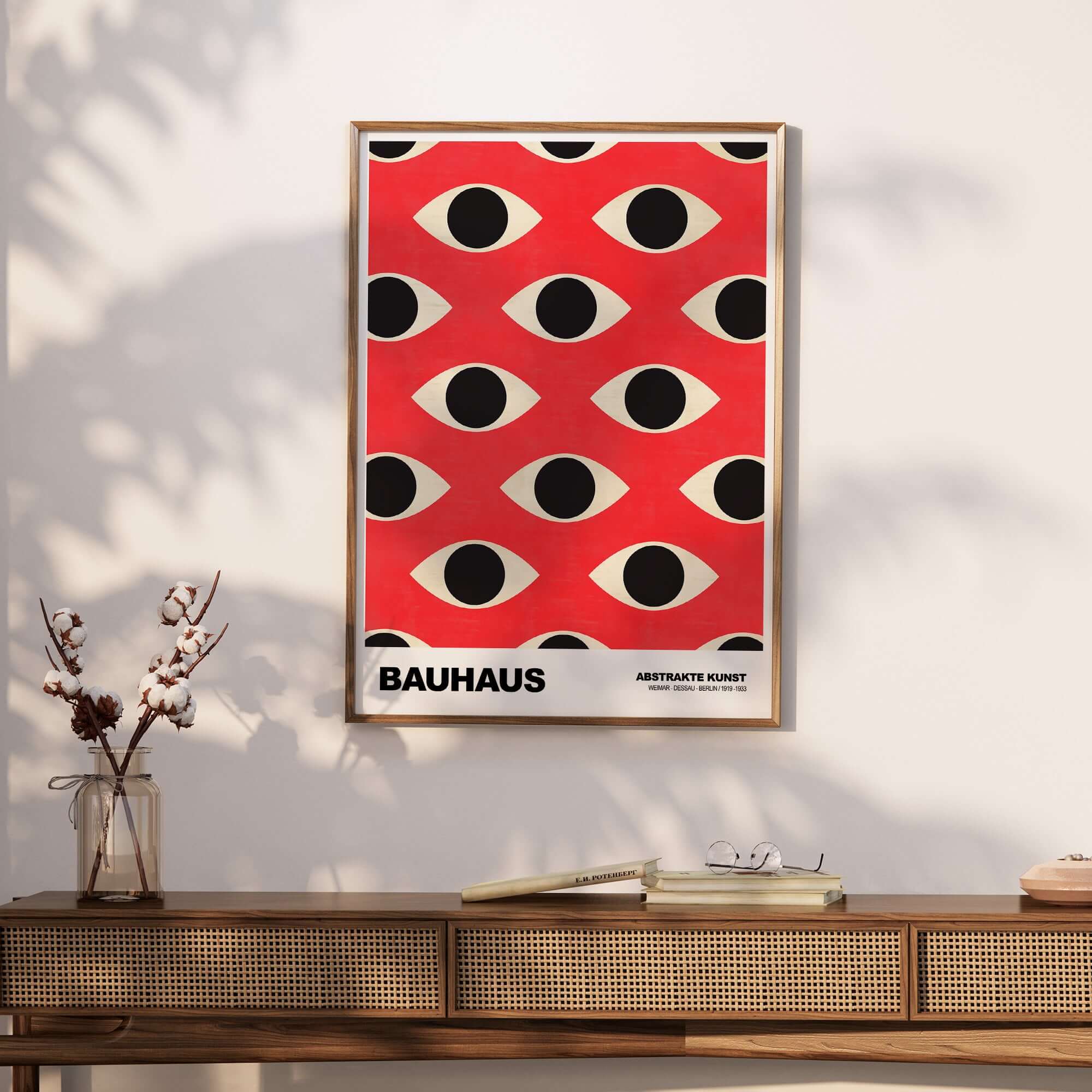 Bauhaus Exhibition Prints - Repeating Eyes Pattern Poster Red Black Cream Art displayed on wall above wooden table.