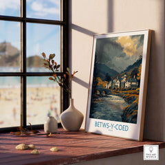 Betws-y-Coed Poster Wales Countryside Landscape Print displayed on a wooden table with a view of the beach.
