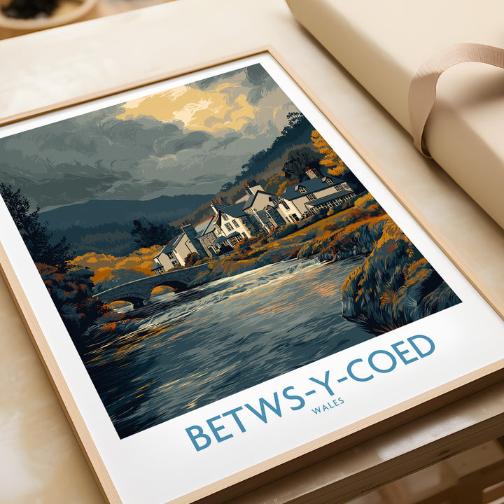 Framed Betws-y-Coed poster featuring a scenic Wales countryside landscape with a river and village homes.